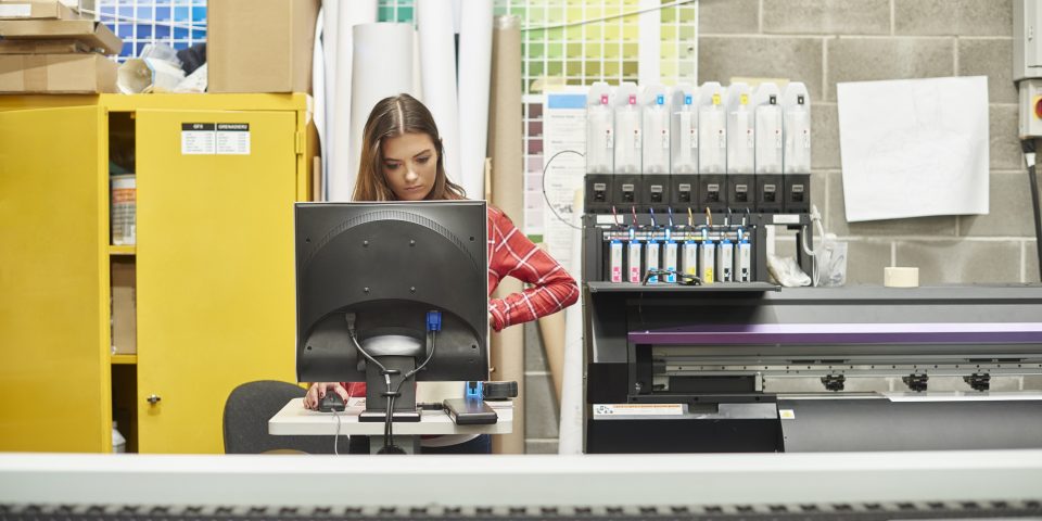 A young woman is working on a digital printing machine.